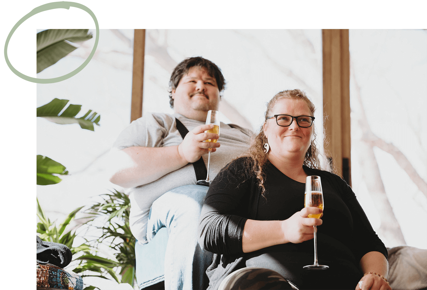 a man and a woman holding champagne glasses sitting in front of a large window