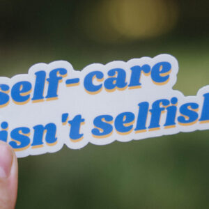 Sticker that says "self-care isn't selfish" held up in front of a green background