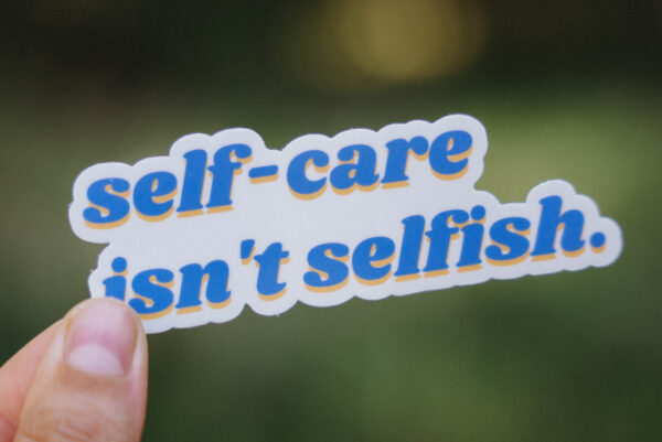 Sticker that says "self-care isn't selfish" held up in front of a green background