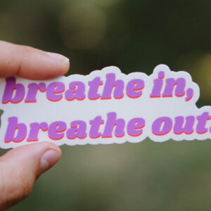 Sticker that says "breathe in, breathe out" held up in front of a green background