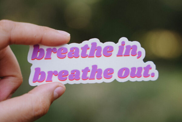 Sticker that says "breathe in, breathe out" held up in front of a green background