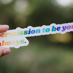 Sticker that says "Permission to be you. Always." held up in front of a green background