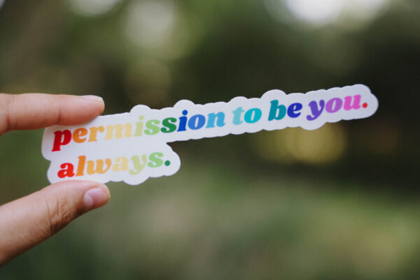 Sticker that says "Permission to be you. Always." held up in front of a green background