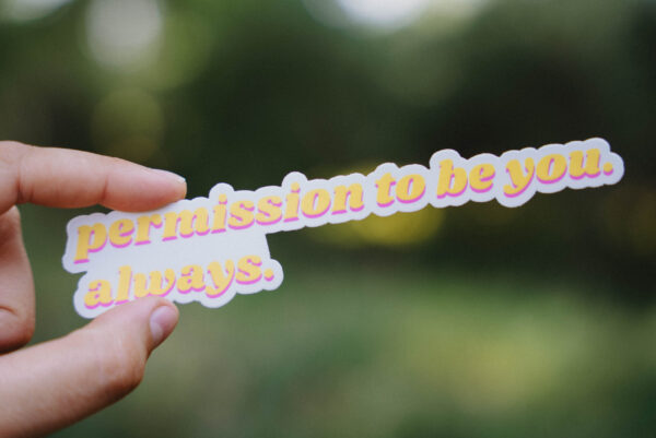 Sticker that says "Permission to be you. Always." held up in front of a green background