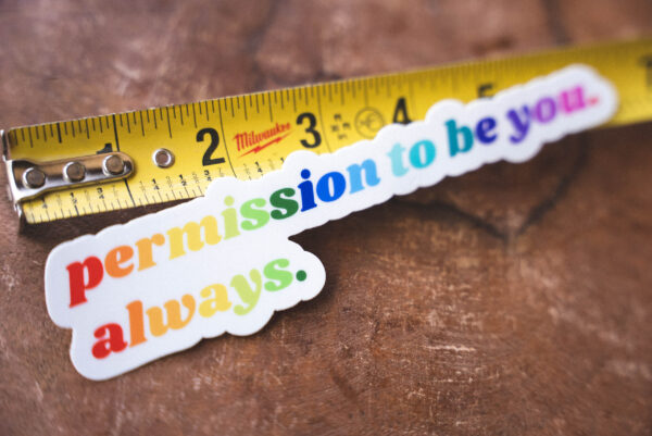 Sticker that says "permission to be you. always." and a tape measure on a table