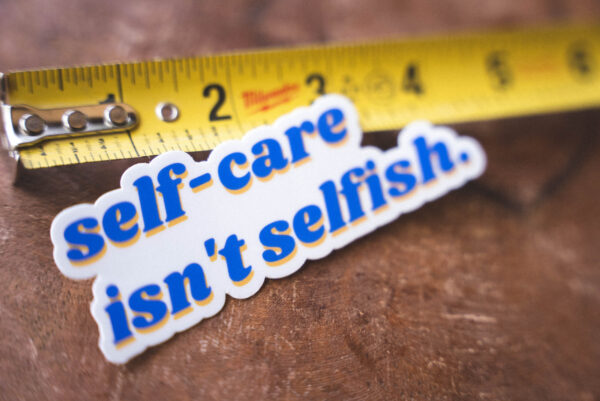 Sticker that says "self-care isn't selfish" and a tape measure on a table