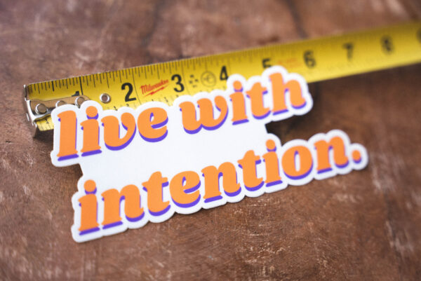 Sticker that says "live with intention" and a tape measure on a table