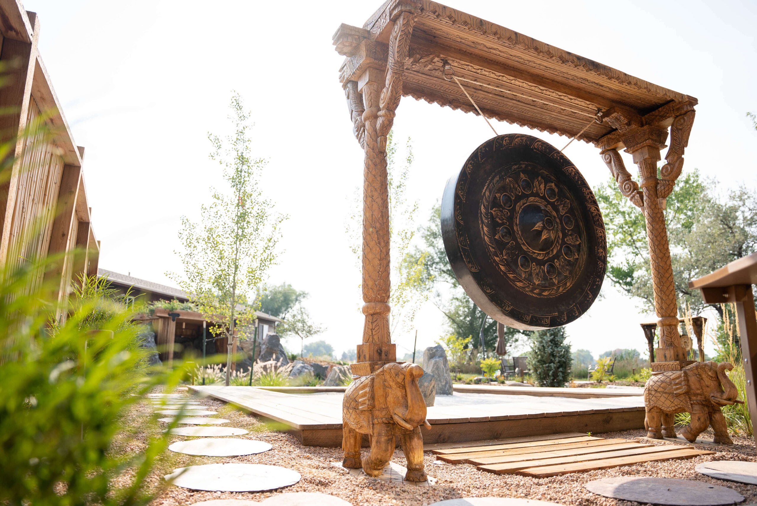 Large gong hanging from wood elephant frame in front of zen garden