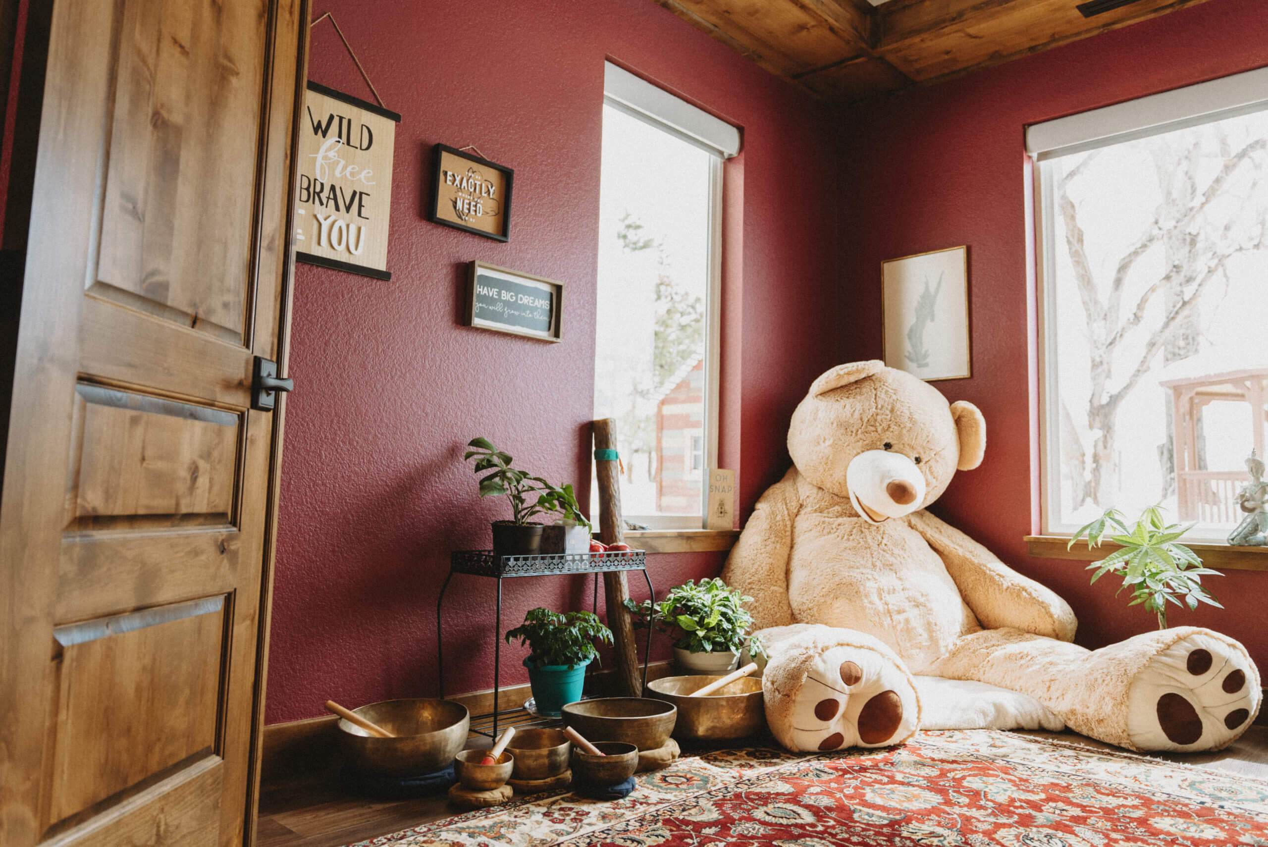 Wide shot of a red room with bright windows and a giant stuffed teddy bear