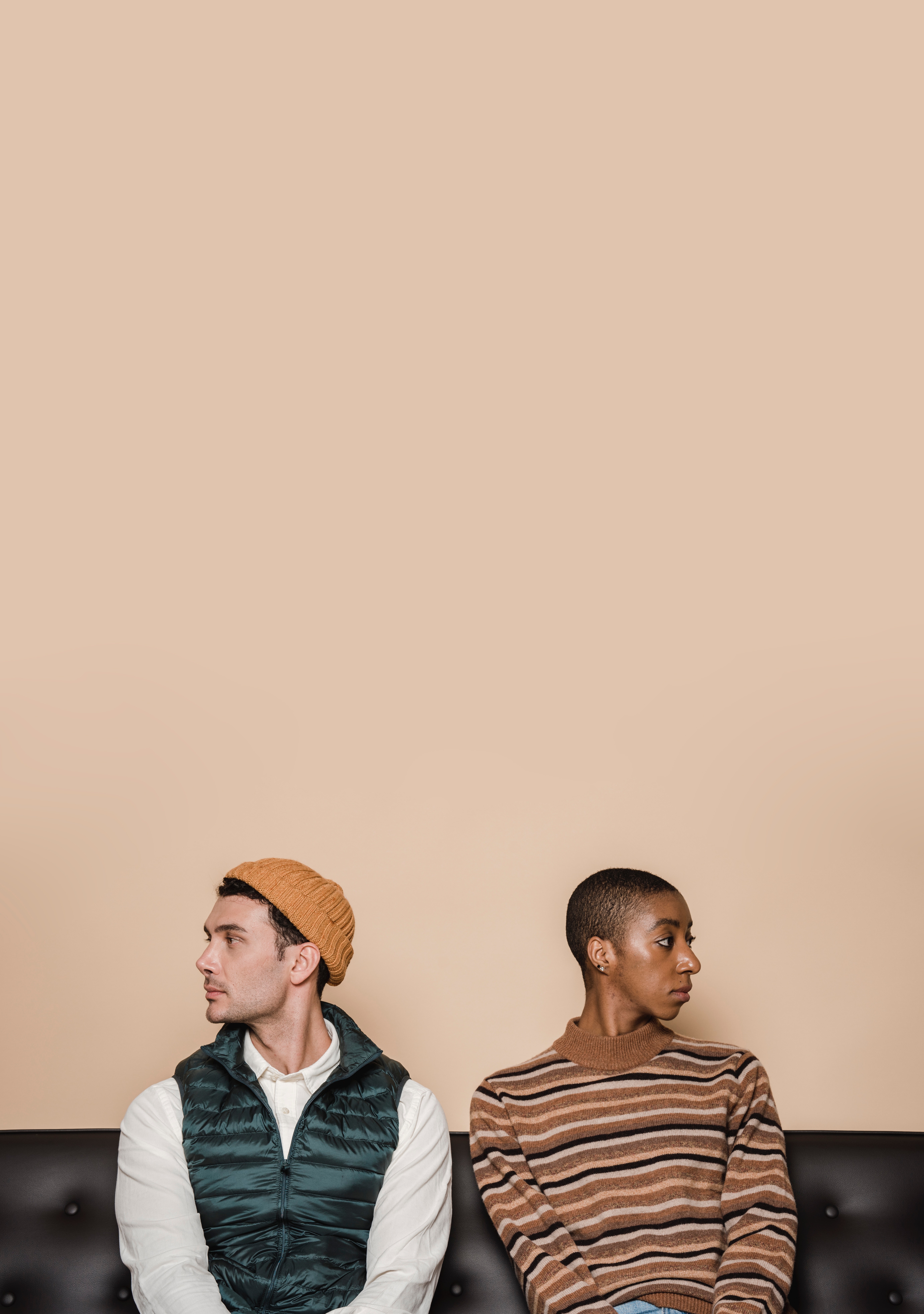 Podcast a man and a woman sitting against a tan wall looking away from each other