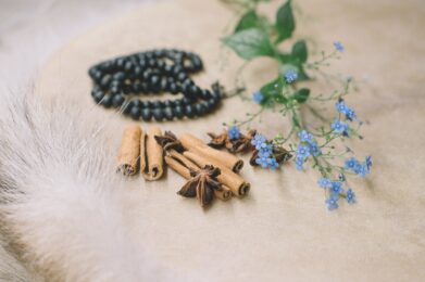 close up of a white feather, black beads, green leaves, and blue flowers on a white surface