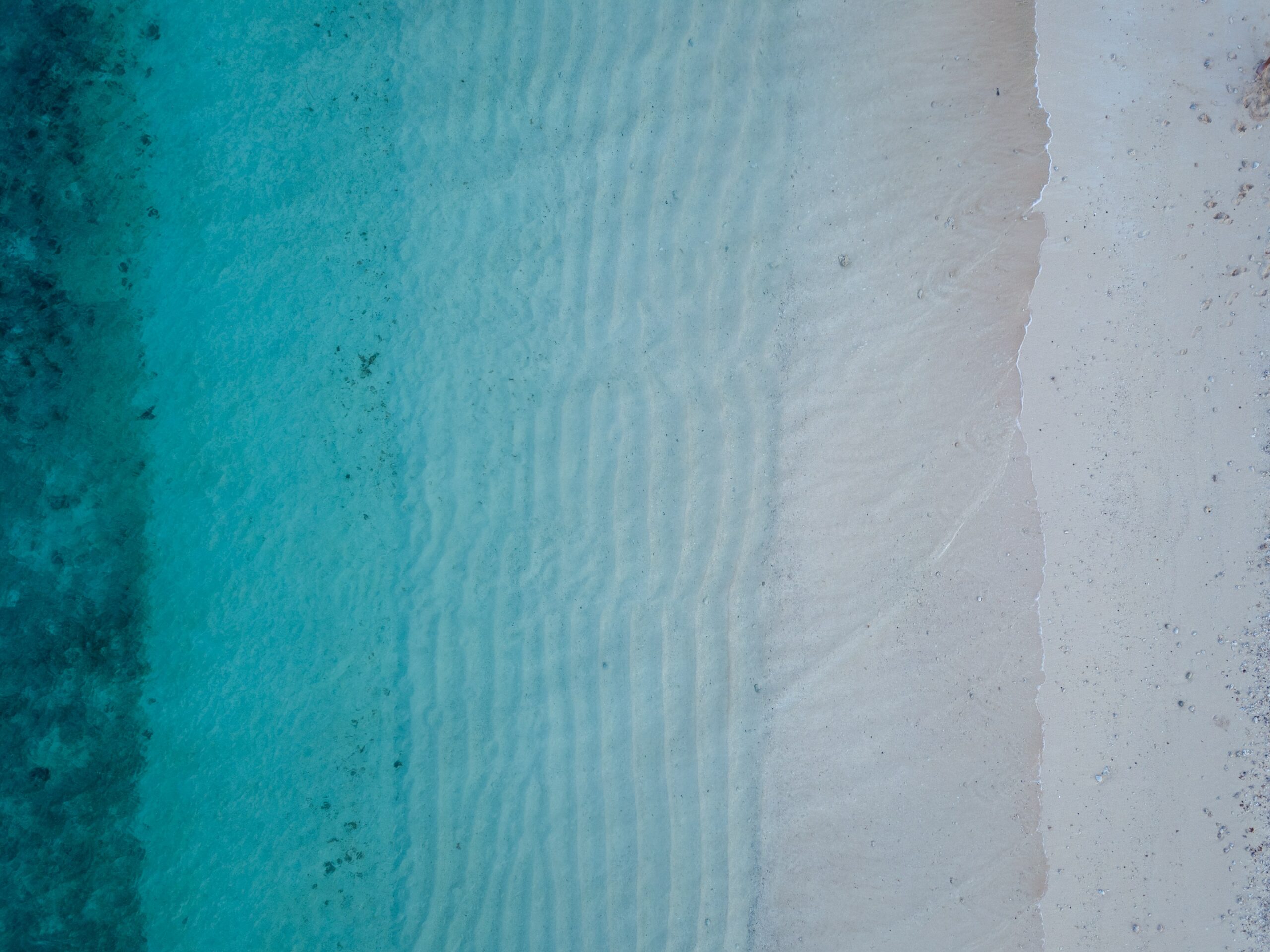 Podcast birds eye view of blue waves gently crashing onto a white sand beach